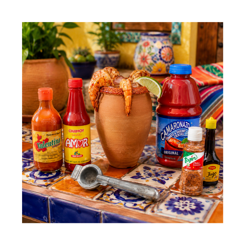 Assorted hot sauce bottles and a margarita on a colorful table with decorative elements.